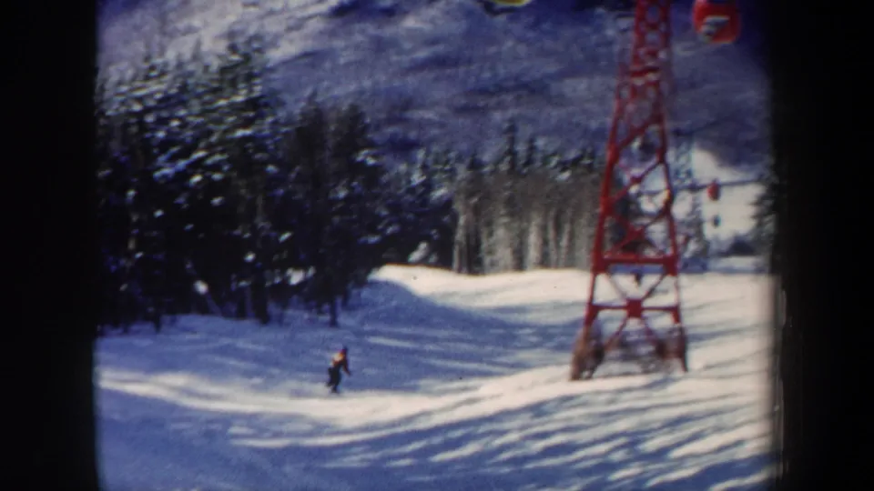 1962 New Hampshire ski-area frame with a skier on a gentle slope, evergreen trees, a red lift tower, and a small cable car overhead.