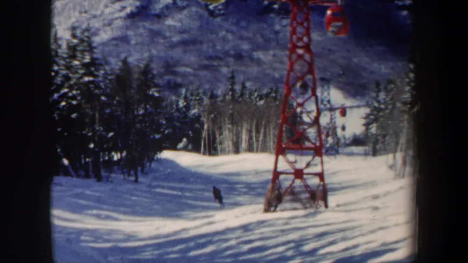 1962 New Hampshire 8mm view of a skier farther down the slope, with blue-shadowed snow, trees, and a red lift tower in frame.