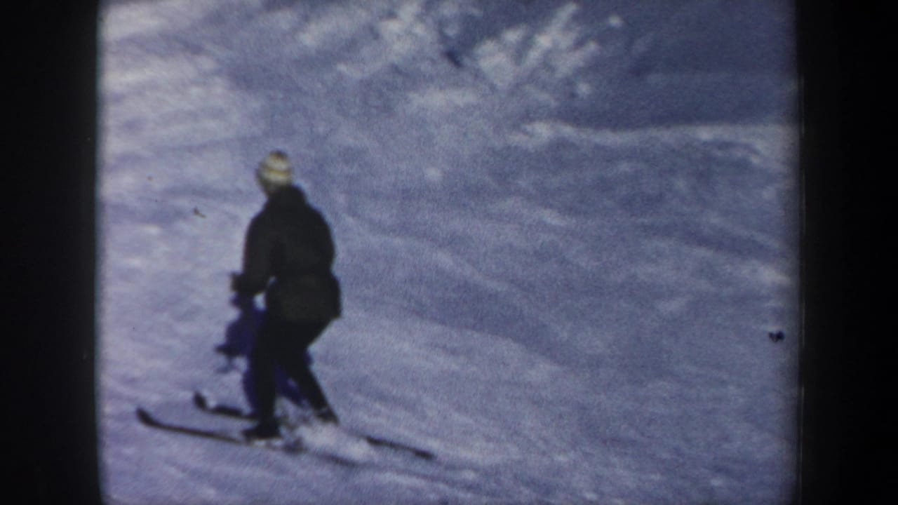 A distant skier in 1962 New Hampshire appears on a snowy slope, wearing a dark coat and light knit hat while holding poles.