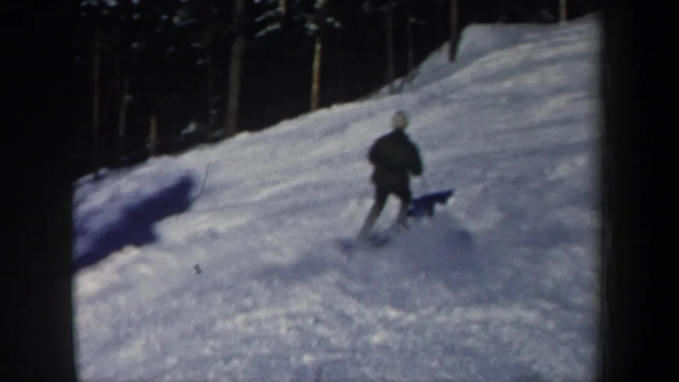 The skier moves downhill across sunlit snow in New Hampshire, with dark evergreen trees bordering the slope.