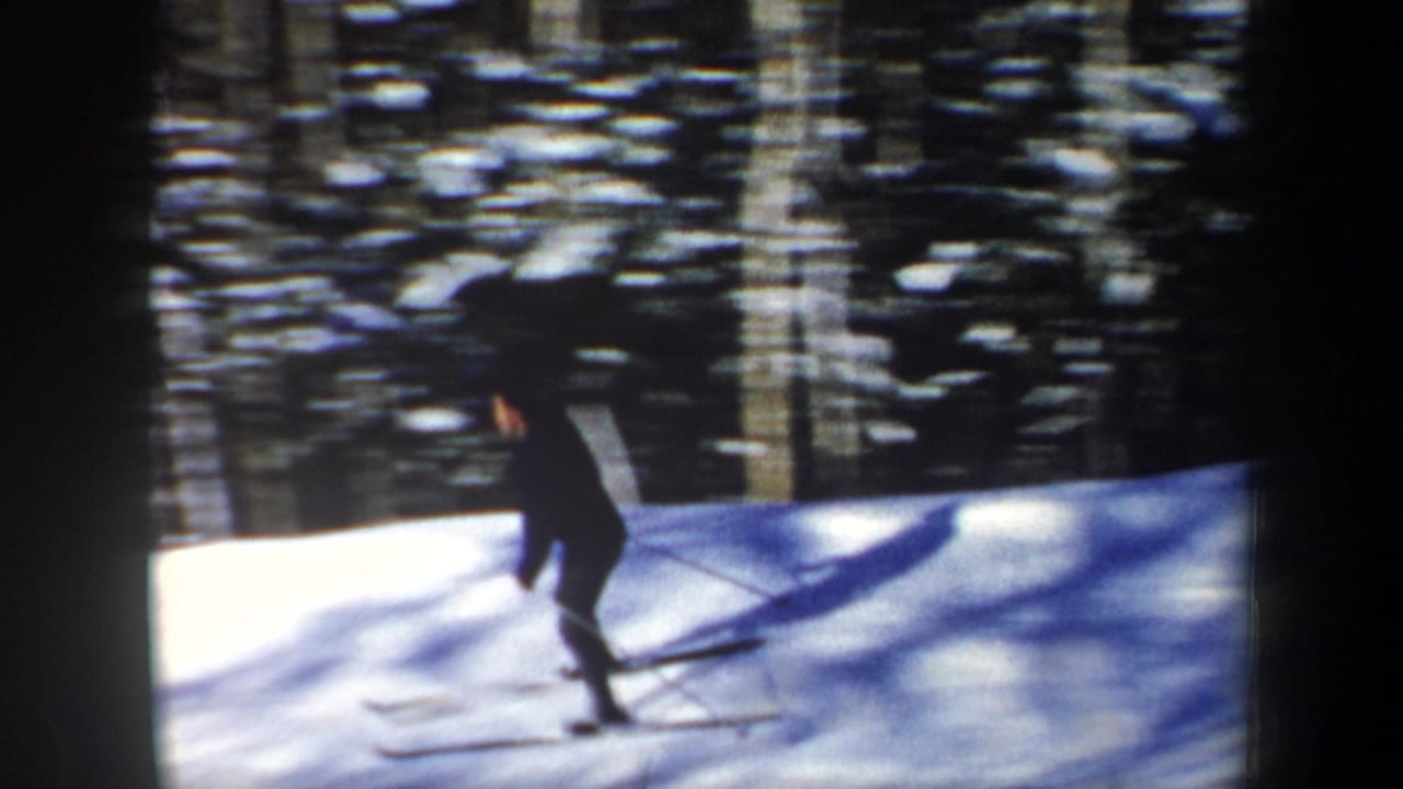 A skier in dark winter clothing crosses a sunlit snow slope before a dense wooded backdrop in the 1962 New Hampshire clip.
