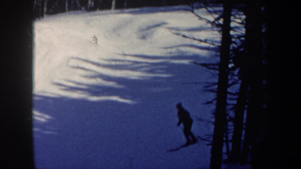 1962 New Hampshire 8mm frame showing a distant skier crossing a bright snowy hillside near shadowed trees.