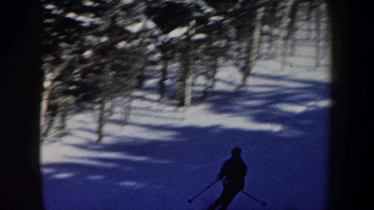 1962 New Hampshire home-movie frame of a skier moving downhill through a blue-shadowed wooded ski area.