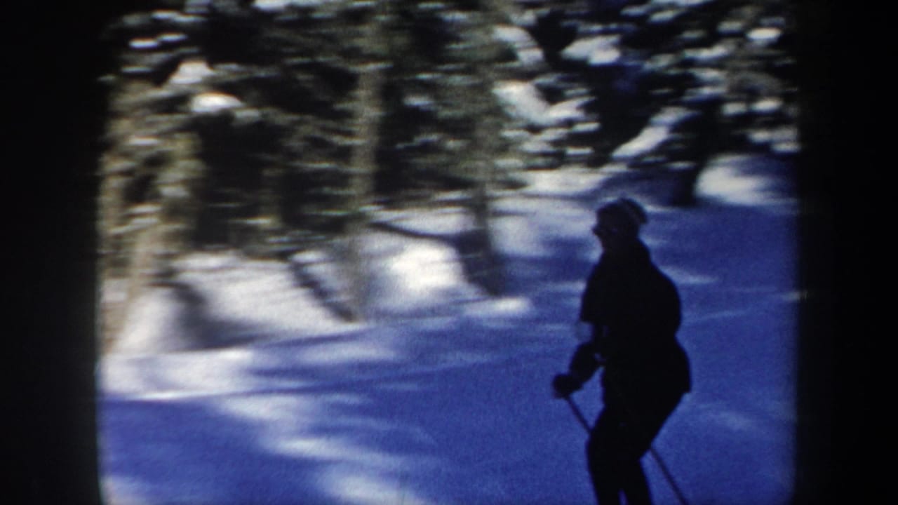 Closer 8mm frame of the skier in winter clothing moving past snowbanks and trees in New Hampshire.