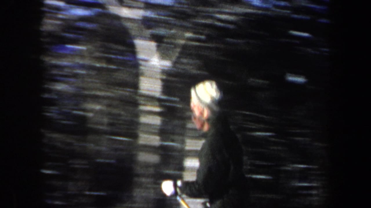 Side-on 1962 New Hampshire frame of a skier in a light knit hat passing a dark wooded background.