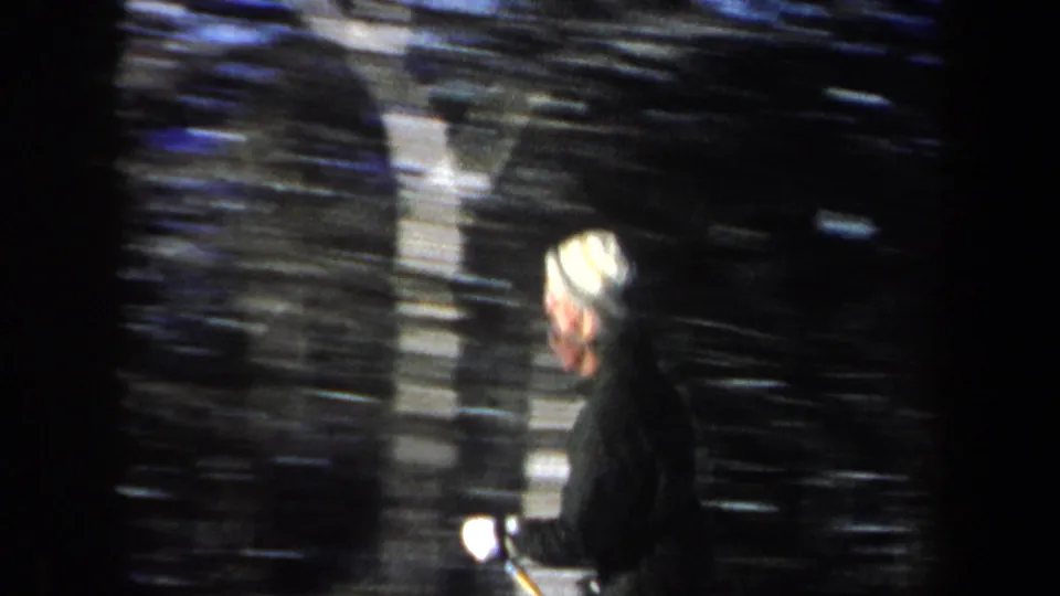 Side-on 1962 New Hampshire frame of a skier in a light knit hat passing a dark wooded background.