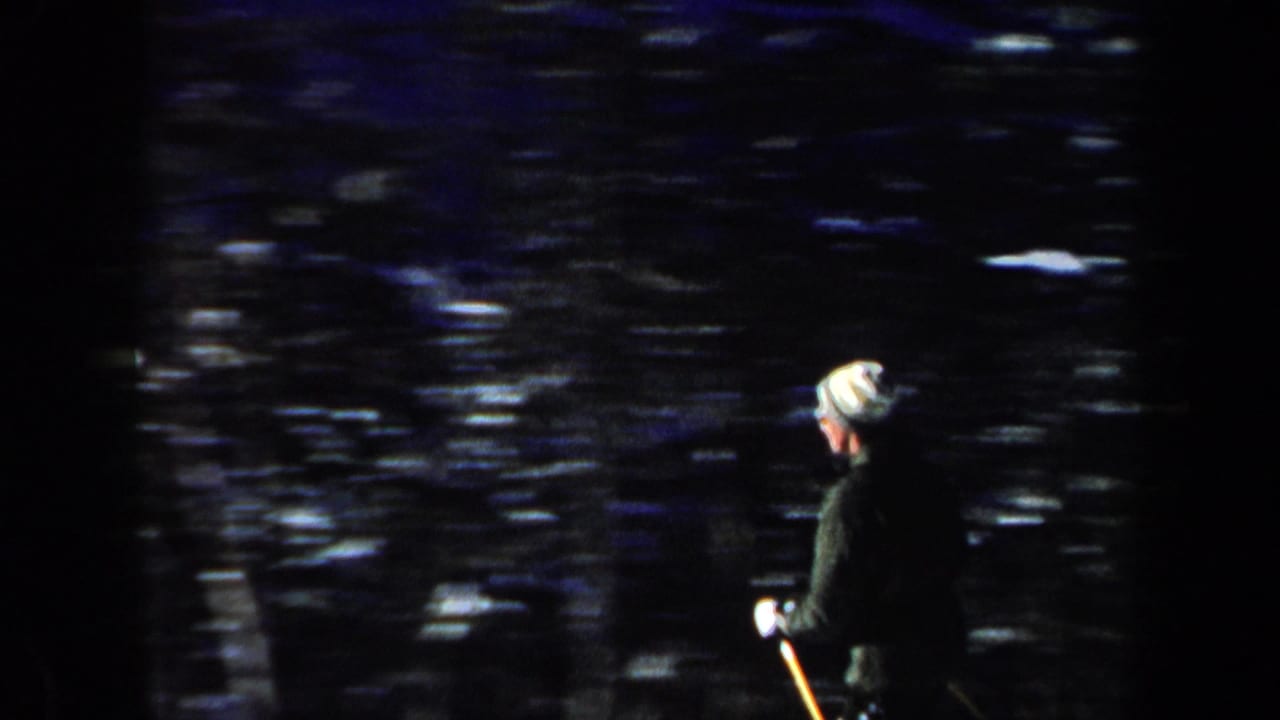 1962 New Hampshire 8mm frame showing a skier in a light hat and dark jacket beside a snowy wooded area.