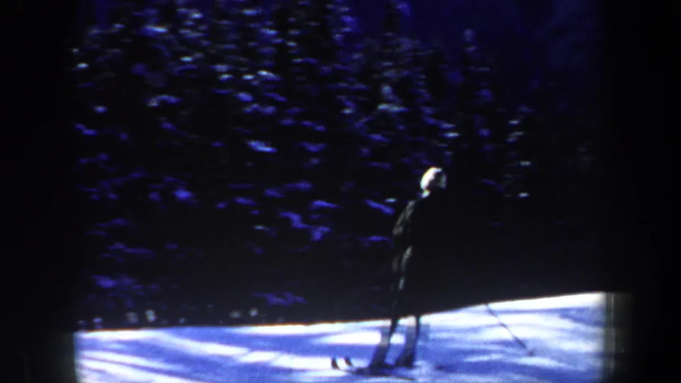 A skier appears at the edge of a bright snowbank with dense evergreen trees behind, in 1962 New Hampshire home-movie footage.