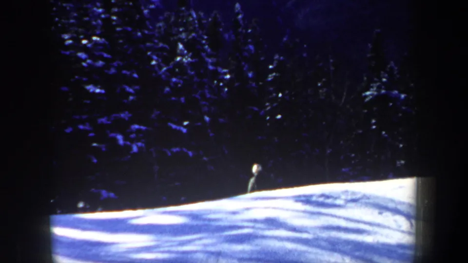 A small skier is visible on a bright snowy slope beneath dense trees in the 1962 New Hampshire winter scene.