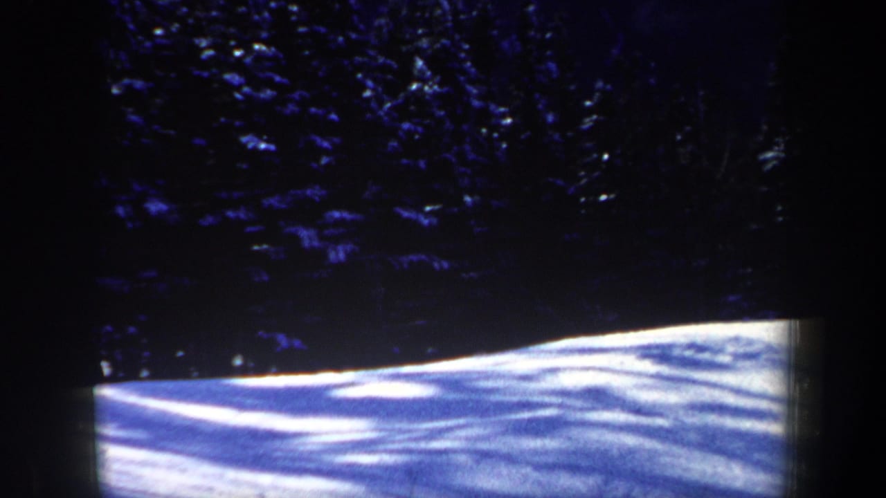 1962 New Hampshire 8mm frame showing a bright snowy slope below shadowed evergreen trees, with no skier clearly visible.
