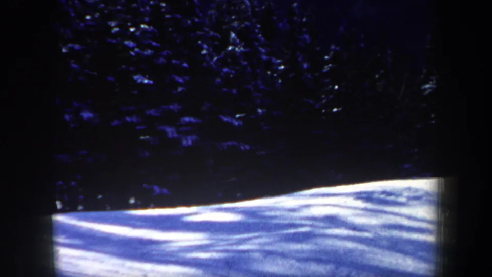 1962 New Hampshire 8mm frame showing a bright snowy slope below shadowed evergreen trees, with no skier clearly visible.