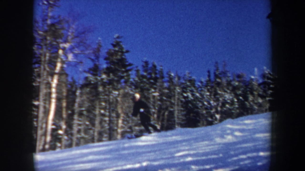 Distant skier on a snowy slope with trees and blue sky behind.