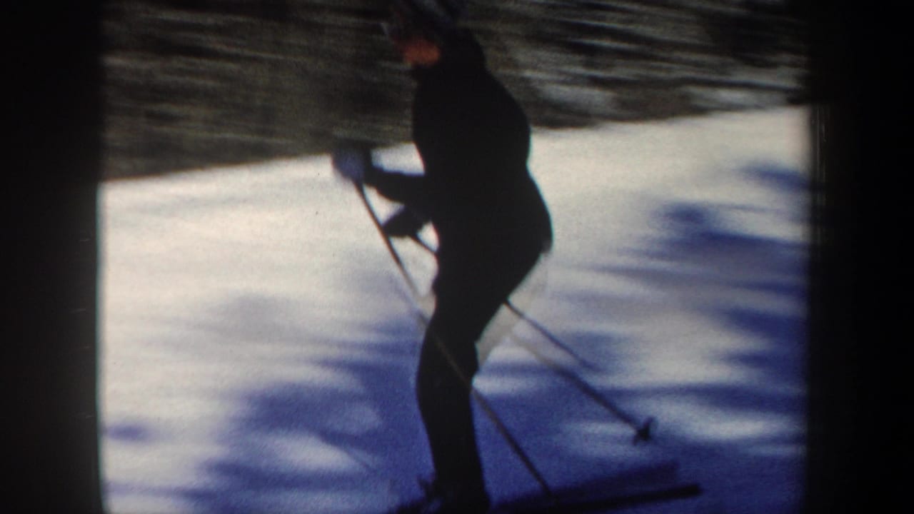 Skier in dark clothing moves across a snowy slope with ski poles.