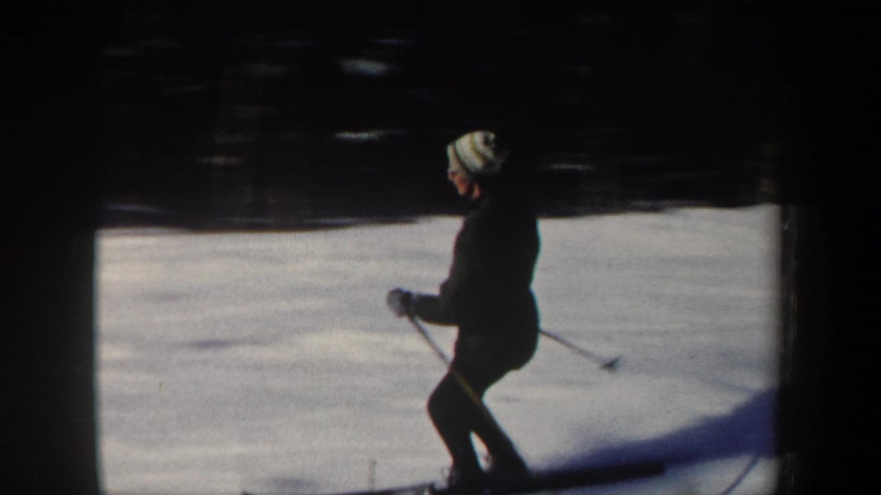 Skier wearing a striped knit hat glides on snow with poles in hand.