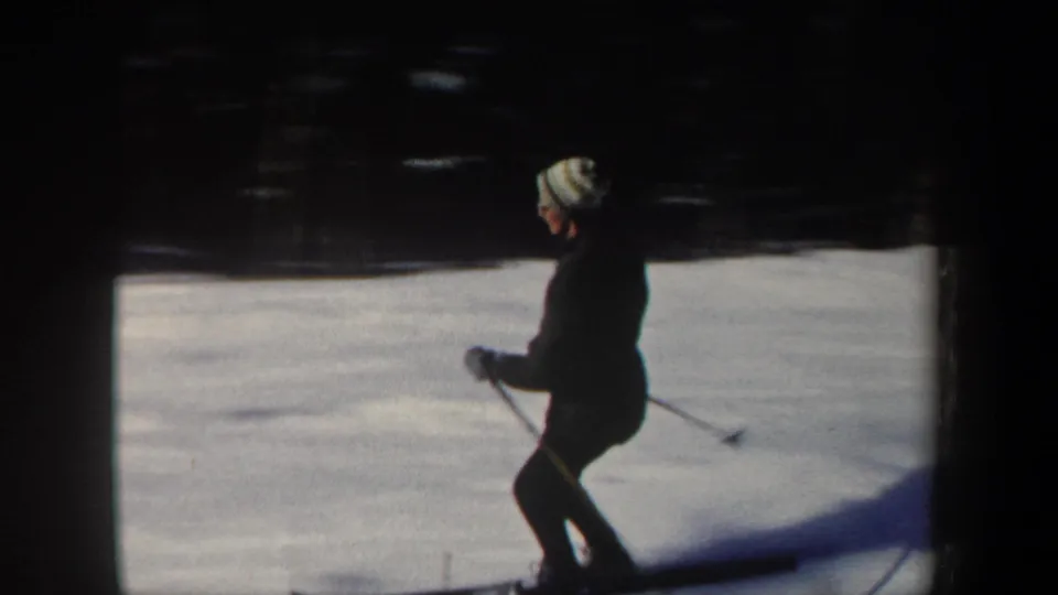 A skier in a striped knit hat and dark coat moves across the snowy hill in the New Hampshire winter scene.