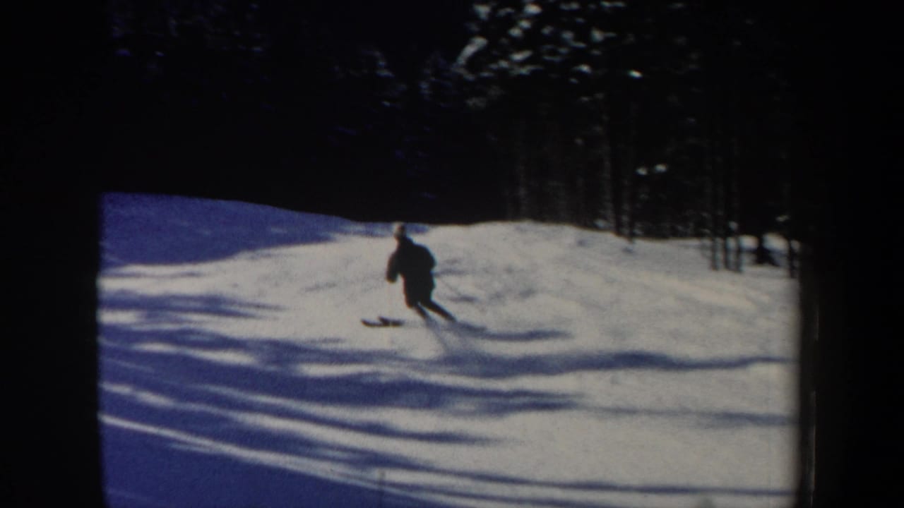A small figure on skis continues downhill across bright snow, framed by dark trees and blue-toned shadows.