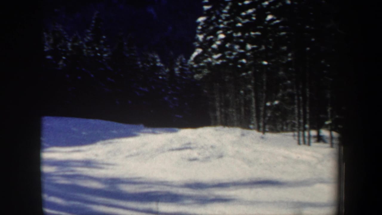 1962 New Hampshire 8mm frame showing a snowy slope, winter trees, blue sky, and dark film-frame edges before the skier enters clearly.