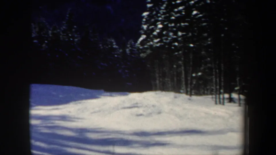 1962 New Hampshire 8mm frame showing a snowy slope, winter trees, blue sky, and dark film-frame edges before the skier enters clearly.