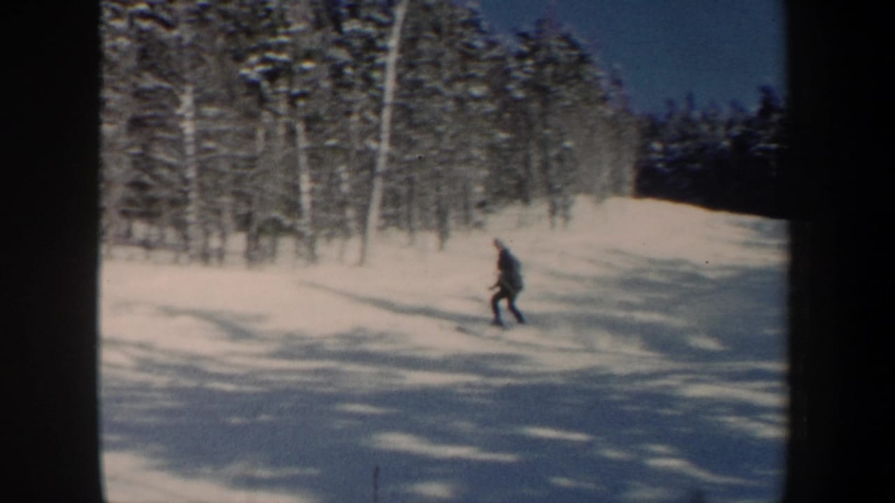 The skier crosses the lower part of a snowy New Hampshire slope, with winter trees, shadows, and visible 8mm frame edges.