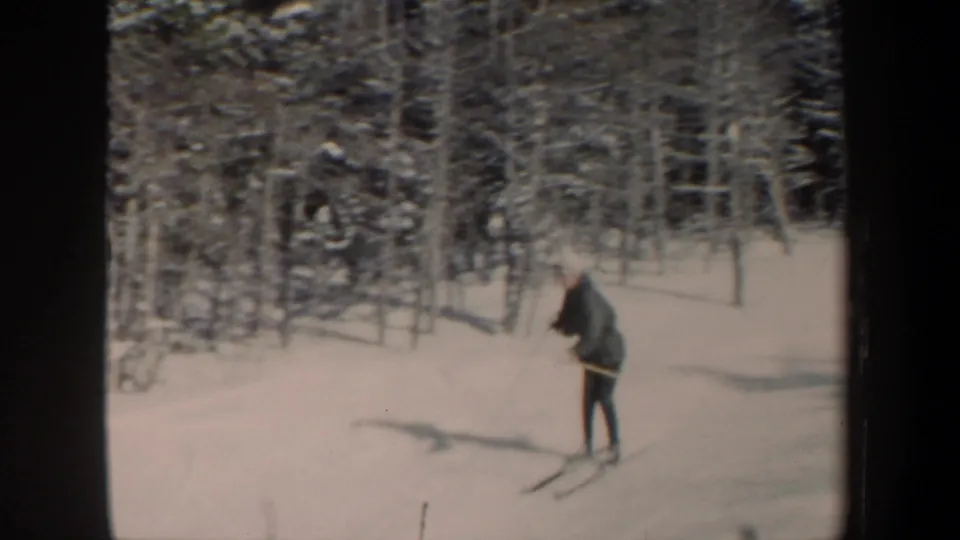 1962 New Hampshire home-movie frame of a skier descending a gentle snowy slope near dense trees.
