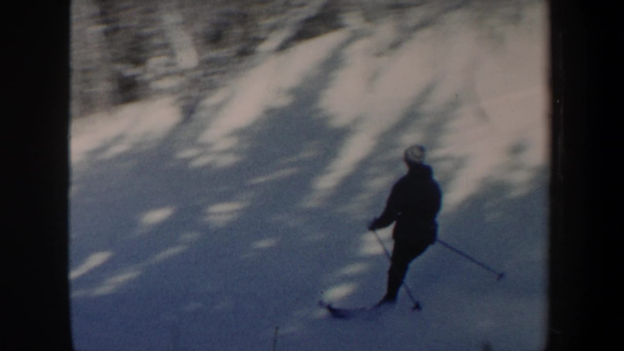Close 8mm view of the skier passing through shadowed snow on a wooded New Hampshire slope in 1962.
