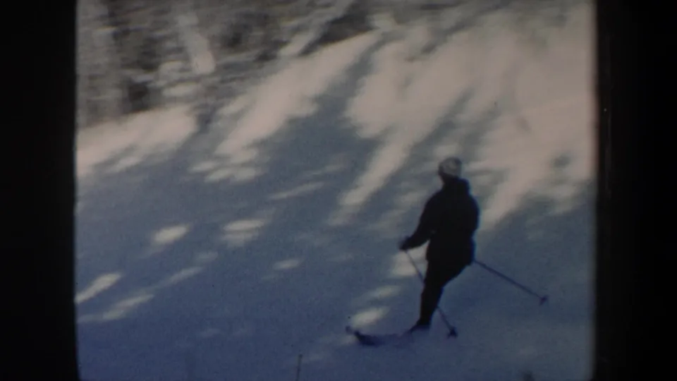 Close 8mm view of the skier passing through shadowed snow on a wooded New Hampshire slope in 1962.