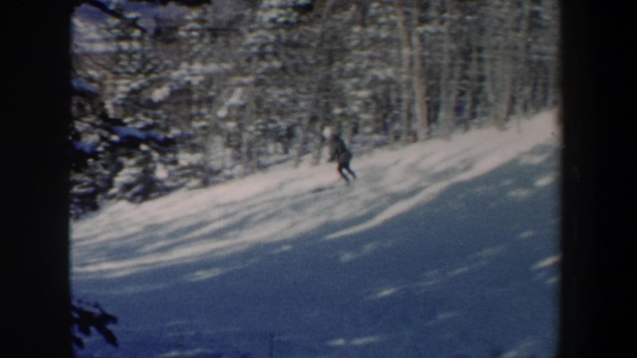 1962 New Hampshire 8mm frame showing a distant skier moving downhill across a snow-covered slope near dense evergreens.