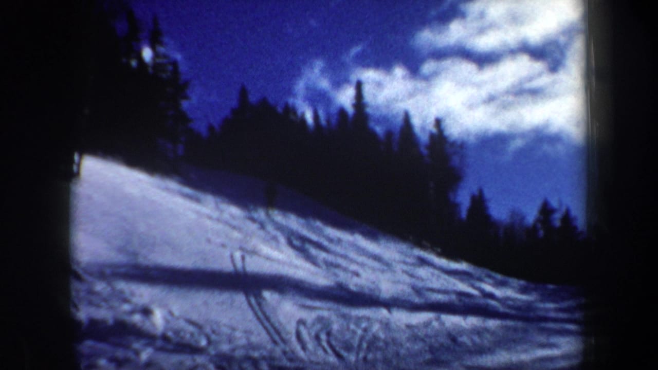 1962 New Hampshire home-movie frame of a snowy hillside, ski tracks, evergreen ridge, and bright blue winter sky.