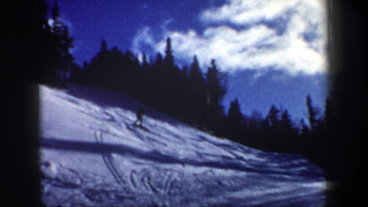 A distant skier crosses a New Hampshire snow slope in 1962 footage, with evergreen trees, ski tracks, and bright sky behind.