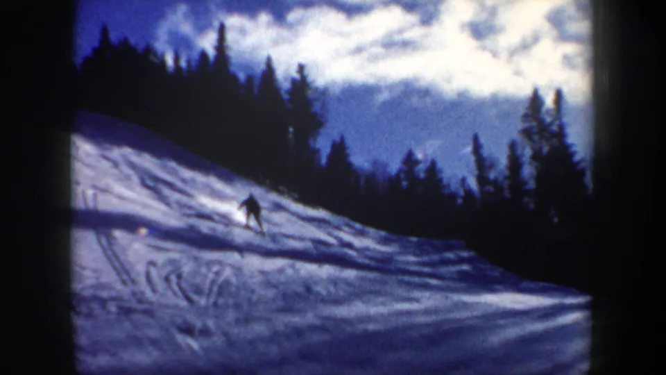1962 New Hampshire 8mm frame showing a lone skier moving down a snowy slope bordered by evergreen trees.