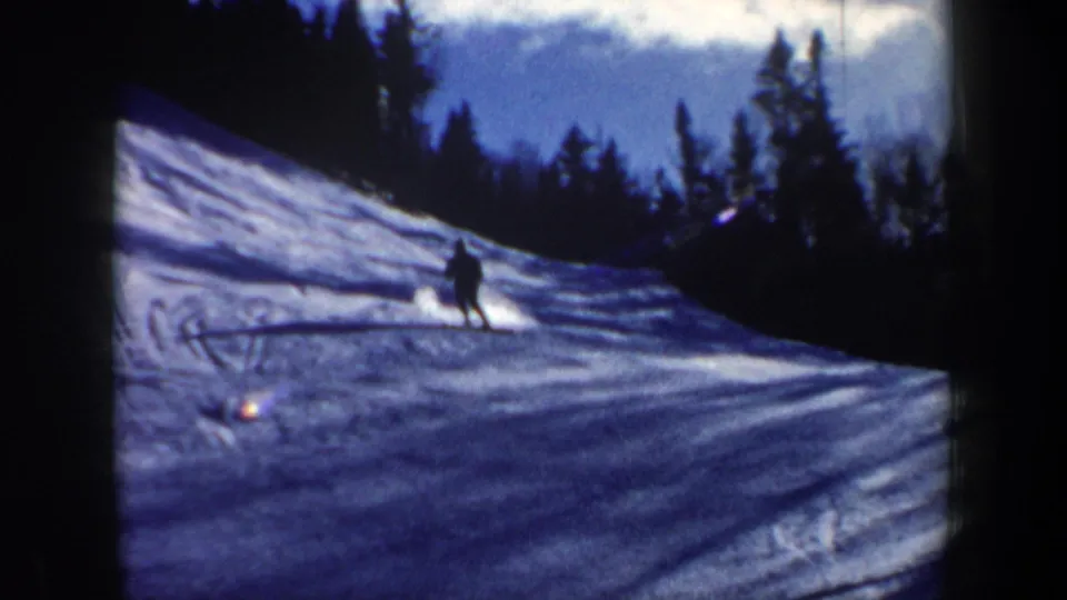 The skier appears mid-descent on a New Hampshire snowy slope, framed by dark evergreens and bright sky.