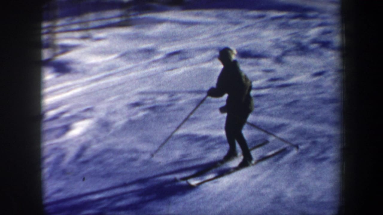 Lone skier in dark winter clothing moves across a snowy slope with poles.