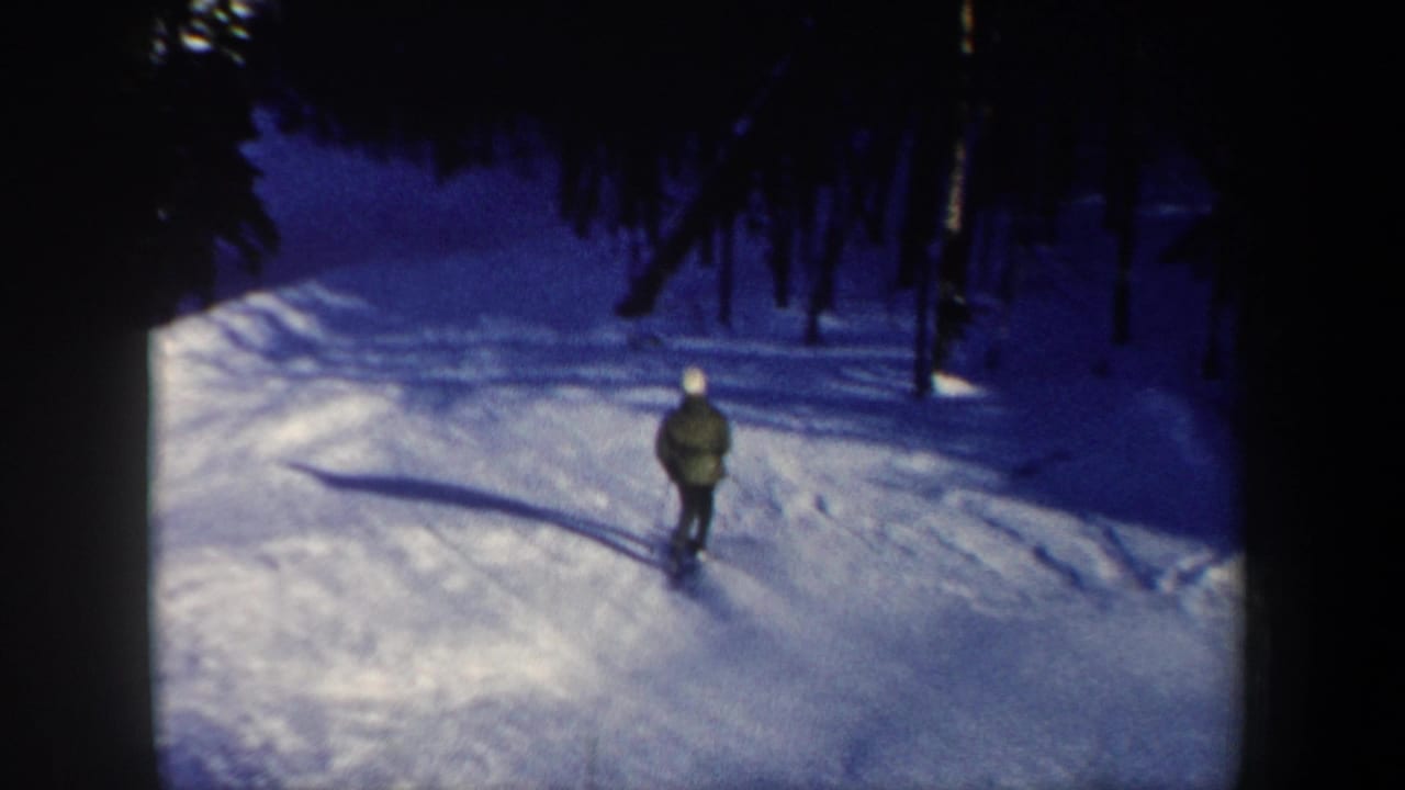 A distant skier continues down a broad snowy trail, with forest shadows framing the route in 1962 New Hampshire footage.