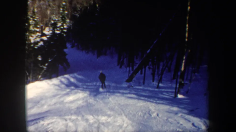 1962 New Hampshire 8mm frame showing a lone skier in dark clothing descending a snow-covered forest slope.