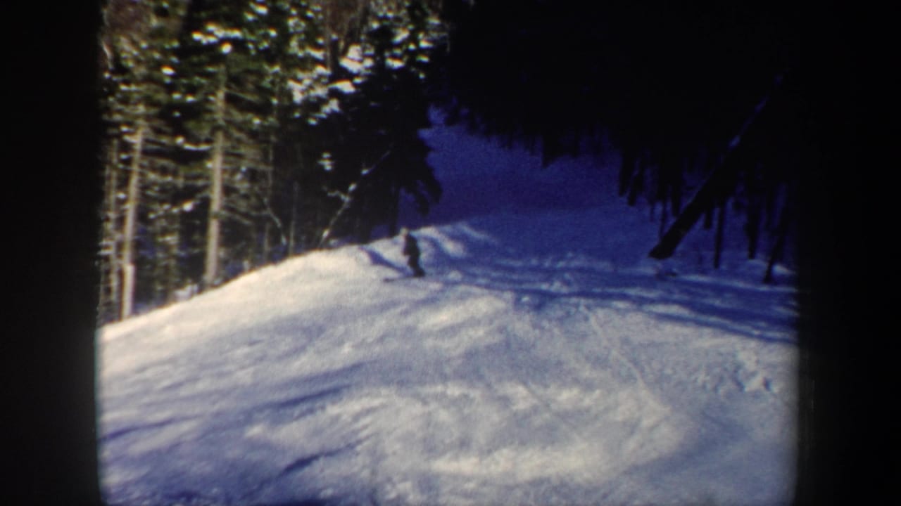 1962 New Hampshire home-movie frame of a skier turning across a sunlit snow slope near dense forest.