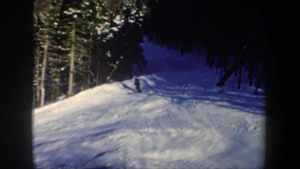 1962 New Hampshire home-movie frame of a skier turning across a sunlit snow slope near dense forest.