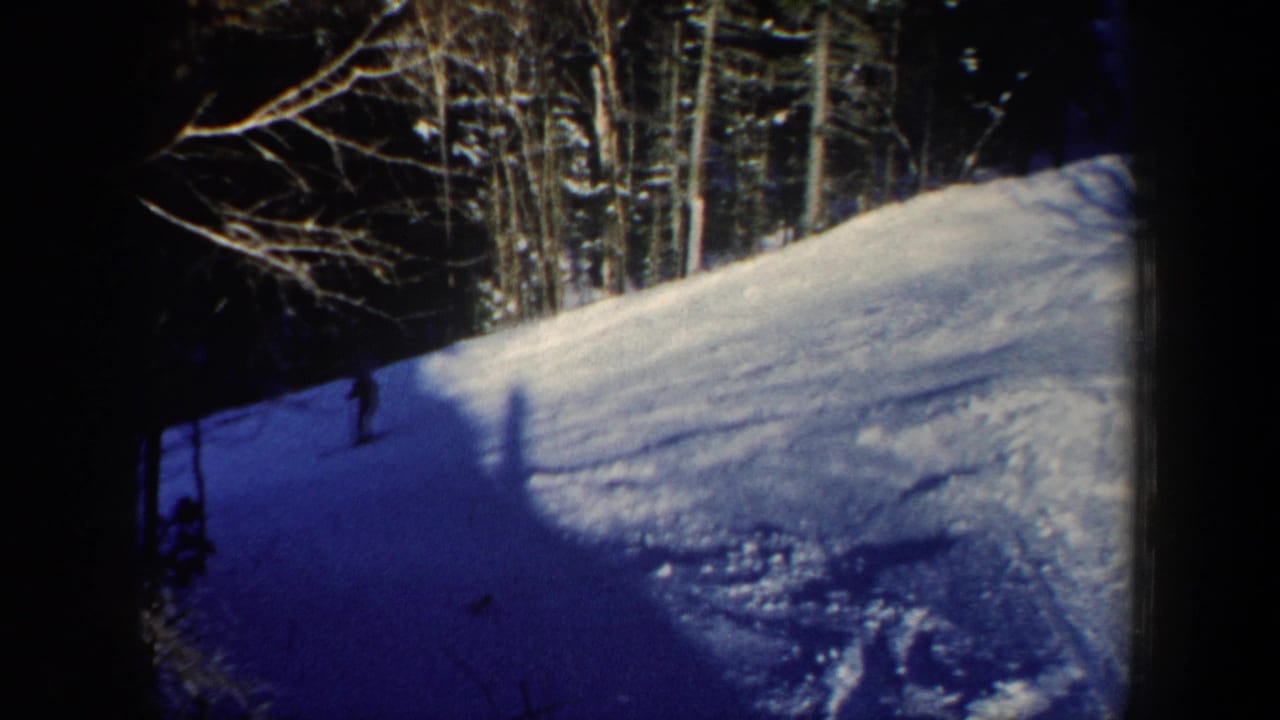 1962 New Hampshire home-movie frame with a lone skier in shadow below a bright snowy forest slope.
