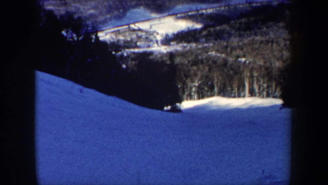 1962 New Hampshire 8mm frame showing a blue-tinted snowy slope, tree line, and distant winter hillside.