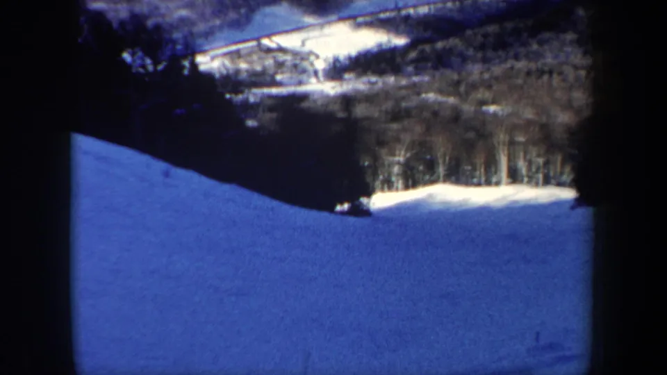 1962 New Hampshire 8mm frame of a broad snowy hillside beneath dark trees and a distant wooded ridge.