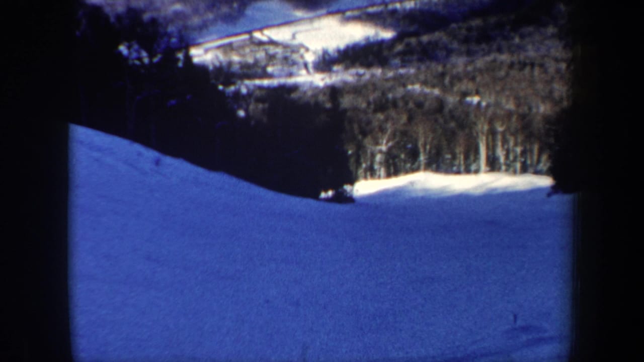 Blue-shifted 1962 New Hampshire 8mm view of a snowy ski slope bordered by winter trees.