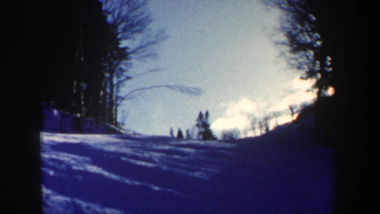 1962 New Hampshire 8mm frame looking up a snow-covered slope toward small distant figures under bright sky.