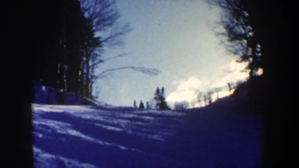 1962 New Hampshire 8mm frame looking up a snow-covered slope toward small distant figures under bright sky.