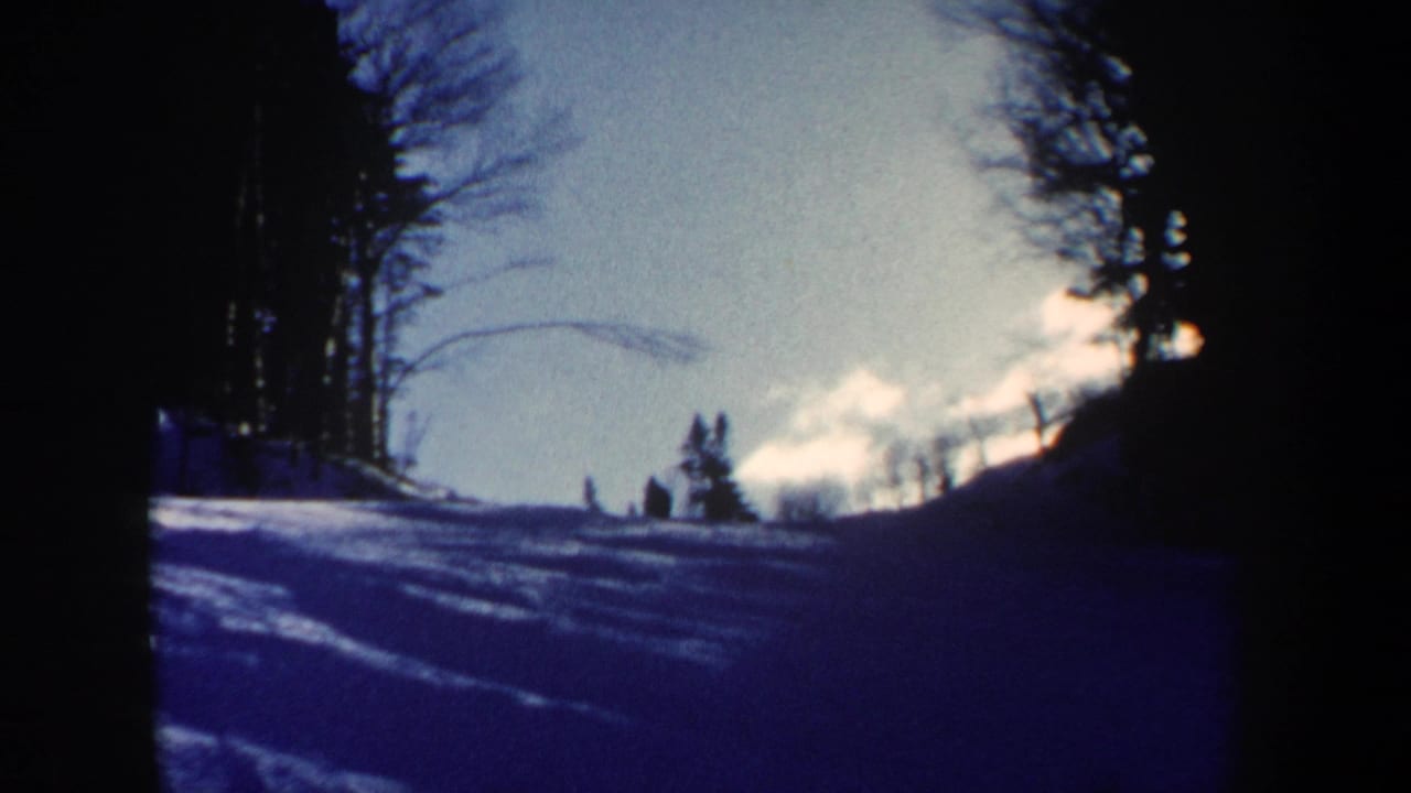 1962 New Hampshire 8mm frame showing a snow-covered ski slope, distant skier silhouettes, bare trees, and strong sunlit winter contrast.