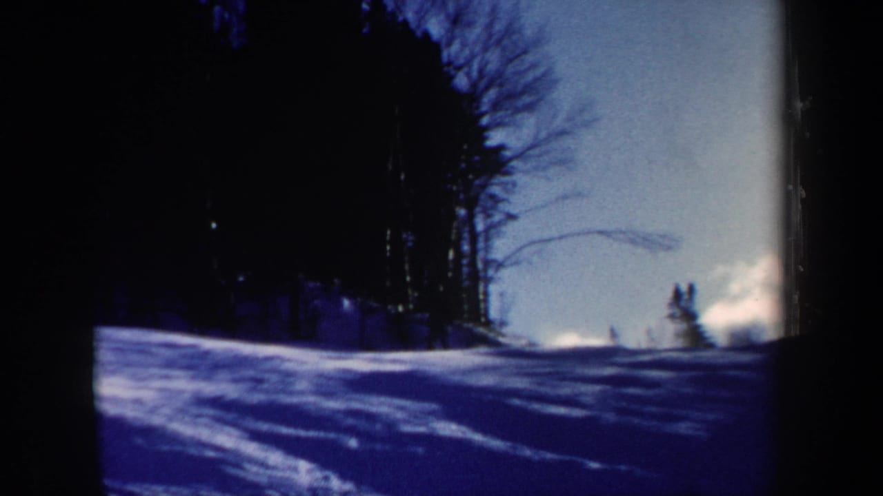 1962 New Hampshire 8mm frame showing the ski slope from a fixed viewpoint, with distant figures and heavy blue shadowing on snow.