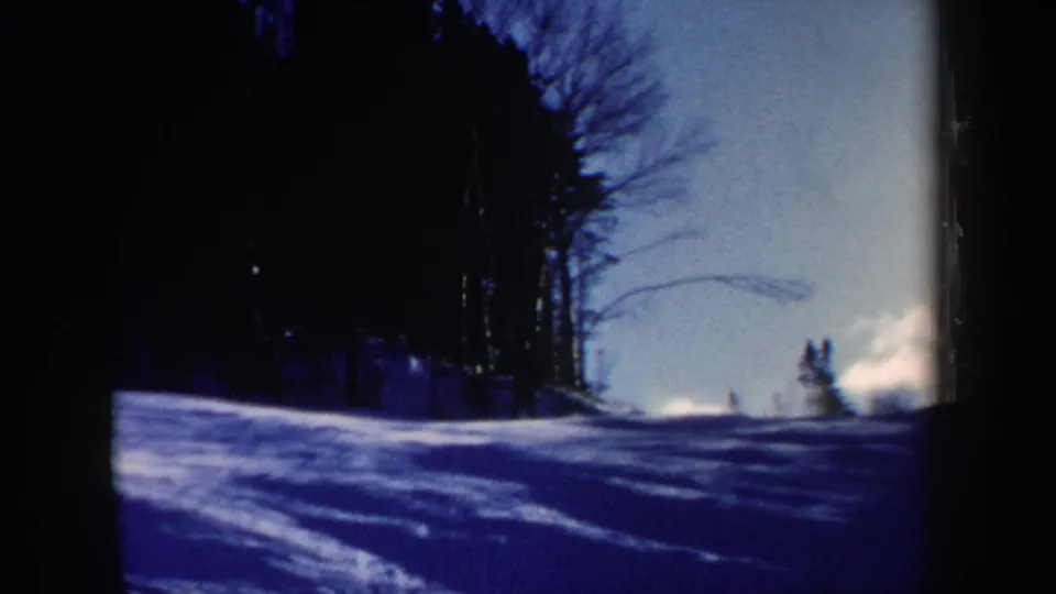 1962 New Hampshire 8mm frame showing the ski slope from a fixed viewpoint, with distant figures and heavy blue shadowing on snow.