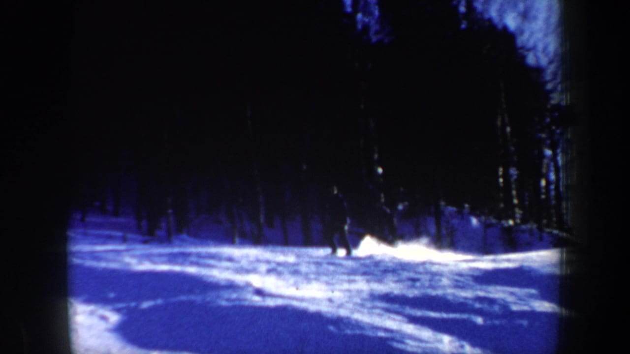 1962 New Hampshire home-movie frame with a more prominent skier silhouette on a bright snowfield, bordered by dense winter trees.