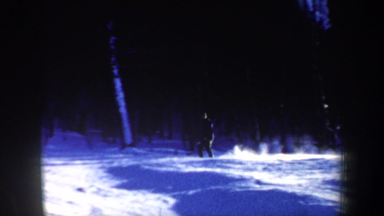 1962 New Hampshire 8mm frame showing a distant skier in dark clothing crossing snowy ground among tall winter trees.
