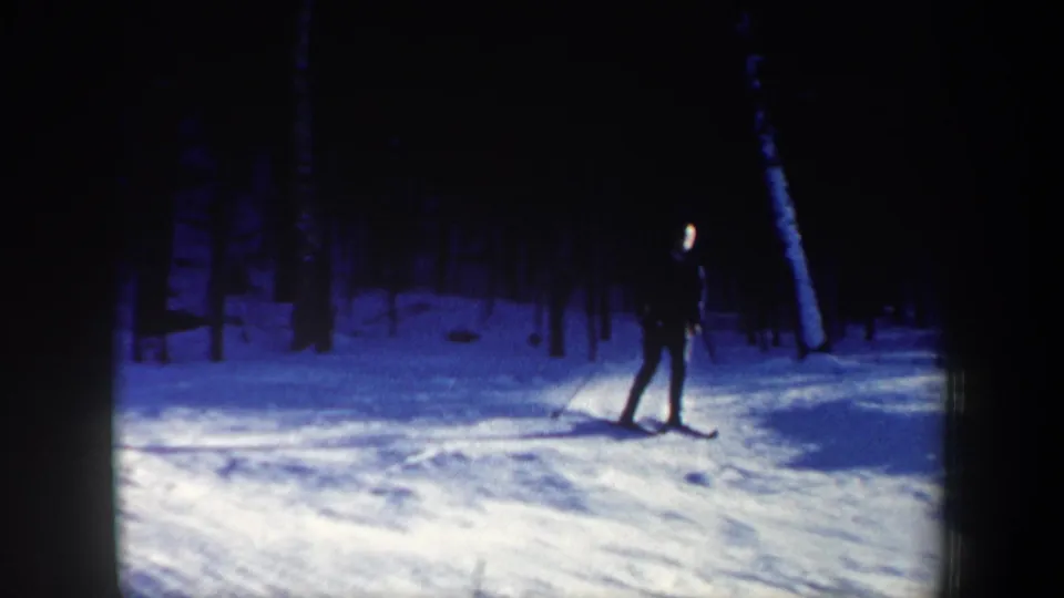 A silhouetted skier moves slowly downhill through a bright snowy New Hampshire forest in this 1962 home-movie frame.