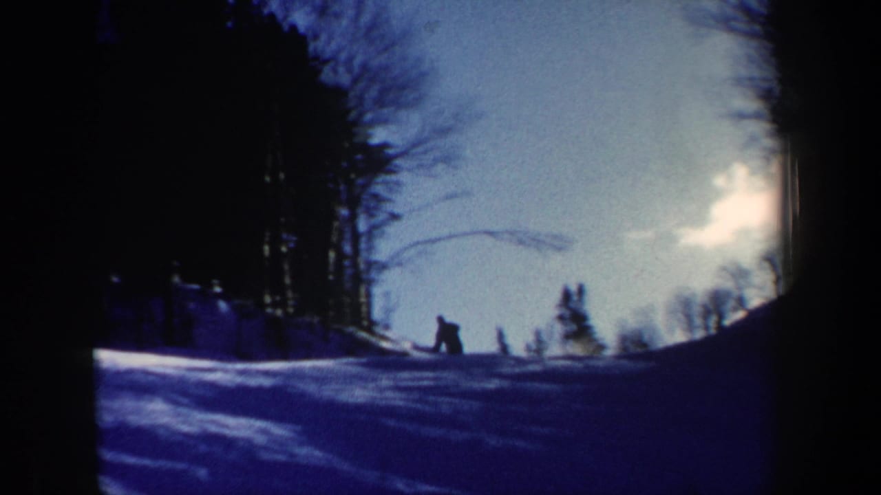 Wide 1962 New Hampshire home-movie frame with a small skier figure on a snowy hillside below bare trees and bright sky.