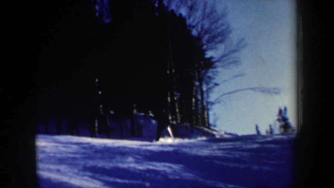 1962 New Hampshire 8mm frame showing a snowy forest slope with a small distant skier and bare trees against a blue winter sky.